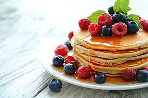 Delicious pancakes topped with fresh berries and drizzled with sweet syrup on a, a Food & Drink Photo by AlyaAnd