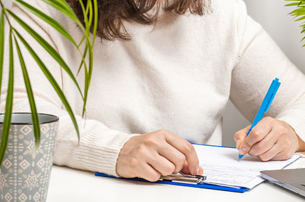 woman in a white sweater and glasses signs documents on the tabl, a Business Photo by ndanko