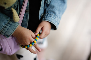 Child wearing a denim jacket holding yellow and blue beaded bracelet, a Person Photo by AS photostudio
