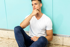Thoughtful young man sitting against turquoise wall, a Person Photo by RF Images