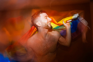 Young adult man smiling celebrating lgbtq+ pride with rainbow flag, a Photo by karrastock