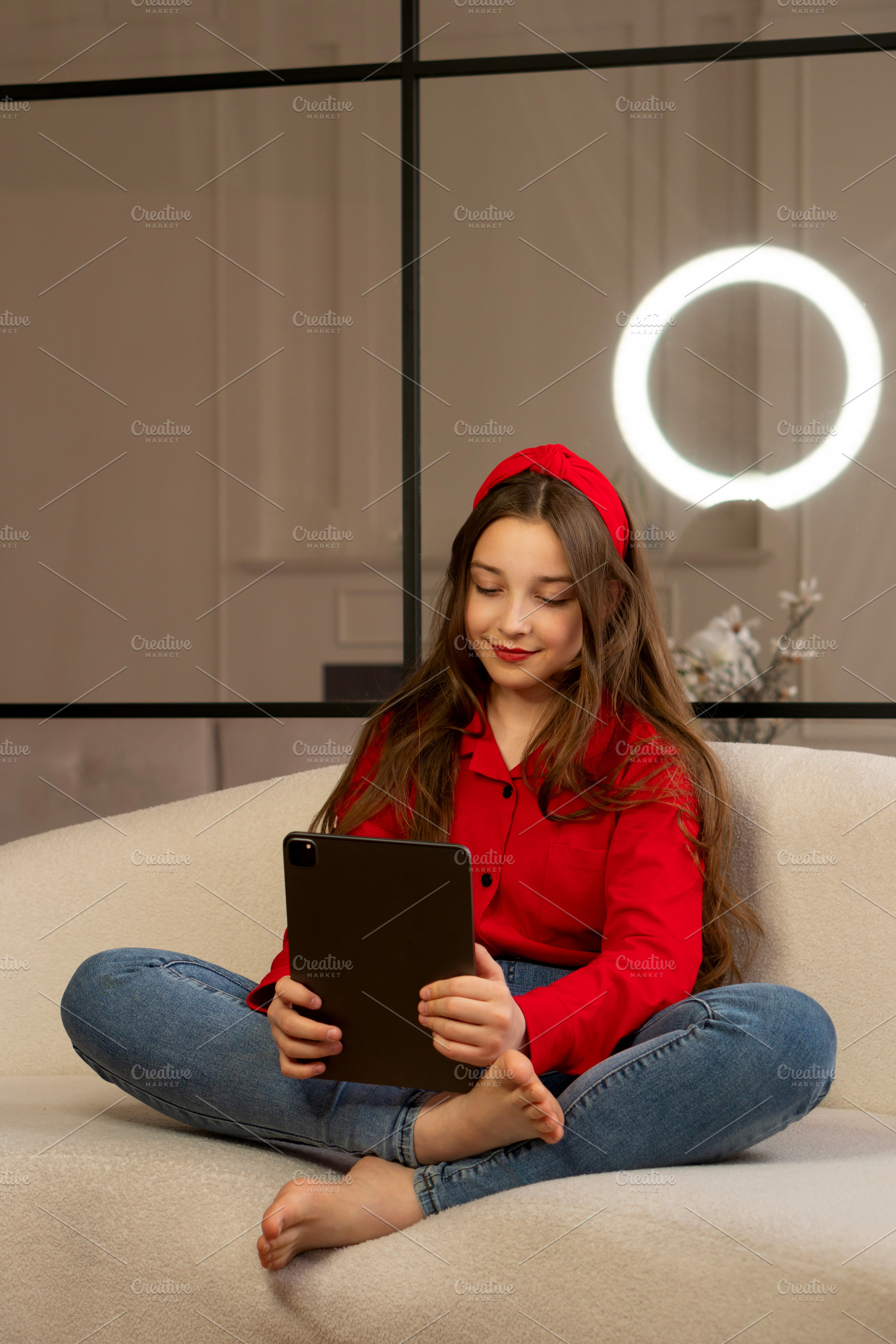 Teen girl sitting cross-legged on so, a Technology Photo by Elena Vagengeim