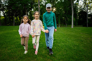 Three smiling children walking together in a park on a sunny day, a Photo by AS photostudio