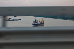 Large cargo ship anchored on a wide river, framed by blurred horizontal bars, w, a Transportation Photo by Ales Munt