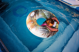 Young girl enjoying summer pool fun with tropical pattern float, a Photo by AS photostudio