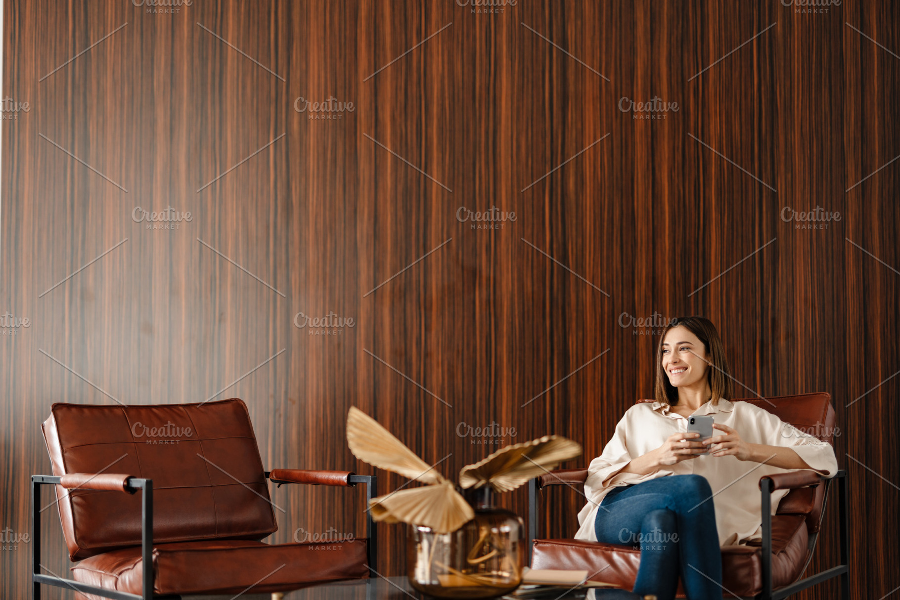 Young smiling woman using cellphone while sitting in armchair indoors, a Person Photo by Dean Drobot
