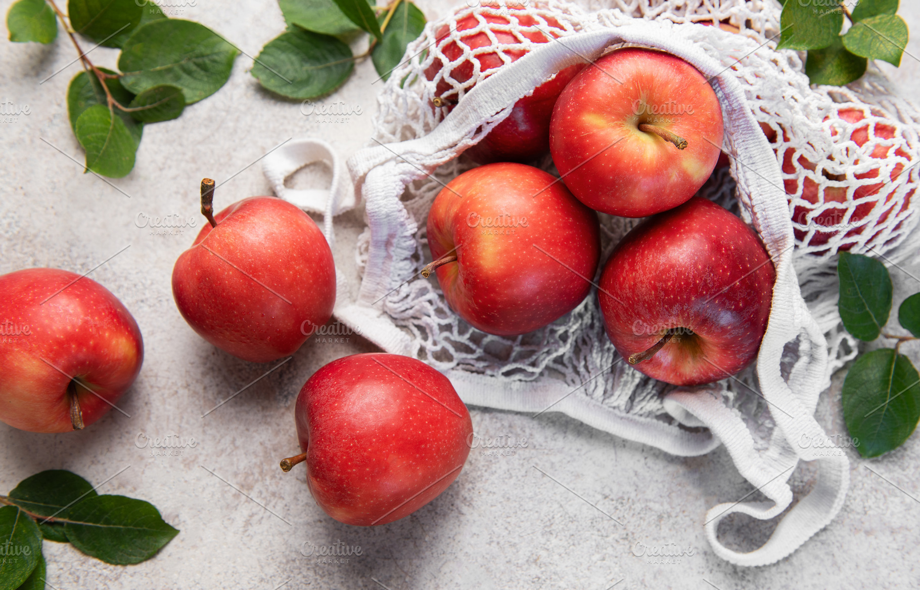Fresh red apples spilling from reusable mesh bag on table, a Food & Drink Photo by Olena Rudo