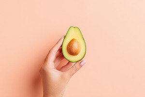 Hand holding a halved avocado on pink background, a Food & Drink Photo by AlyaAnd