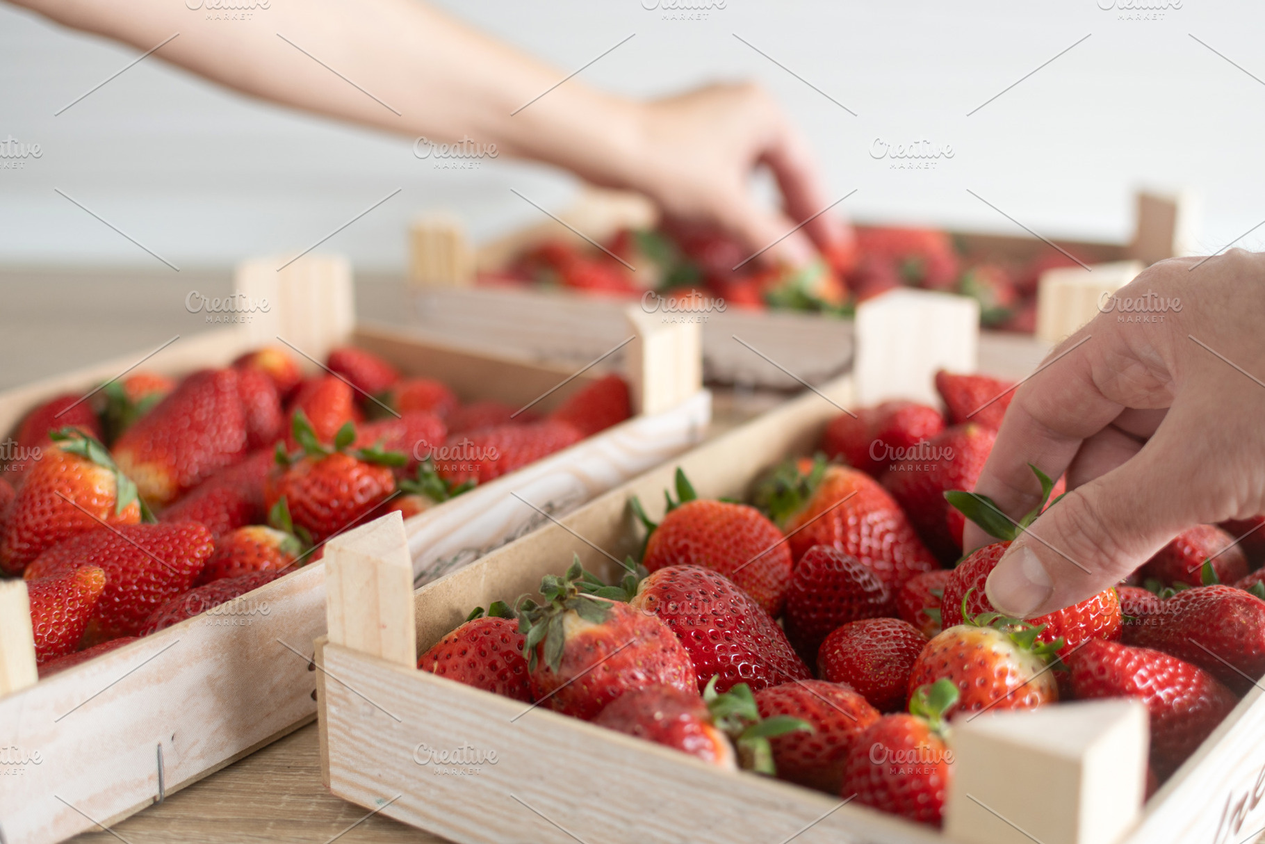 Hands selecting fresh strawberries in wooden crates on table, a Food & Drink Photo by etorres69
