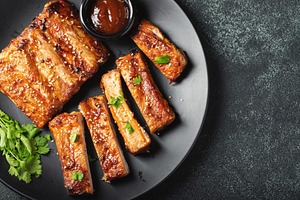 Hot grilled spare ribs from a summer BBQ served on a plate with sauce. Top view, a Food & Drink Photo by Budarinphoto