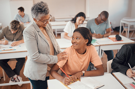 Teacher, student and classroom for test, knowledge and learning for higher education. Young female, black woman or educator helping pupil in exams, talking or students writing notes in books or focus, a Photo by Peopleimages.com