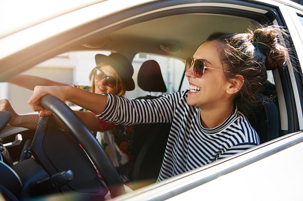 Two laughing young girlfriends driving together in a car, a Person Photo by Stefan & Janni