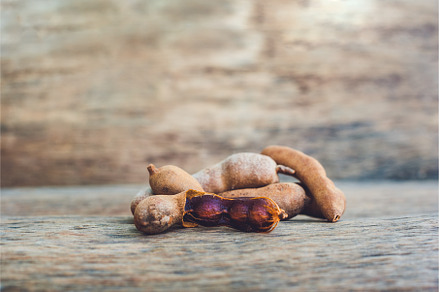 Sweet ripe tamarind pods on old wood, a Food & Drink Photo by Elizaveta Galitskaya