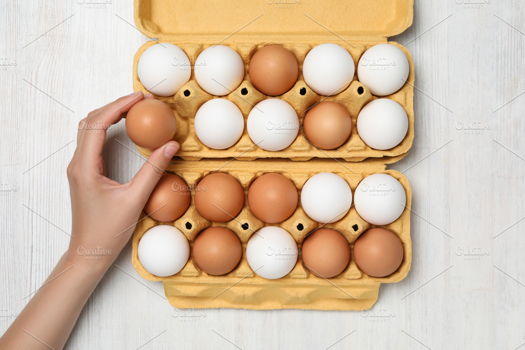 Female hand and egg boxes on white wooden background, a Food & Drink Photo by AtlasStudio PRO