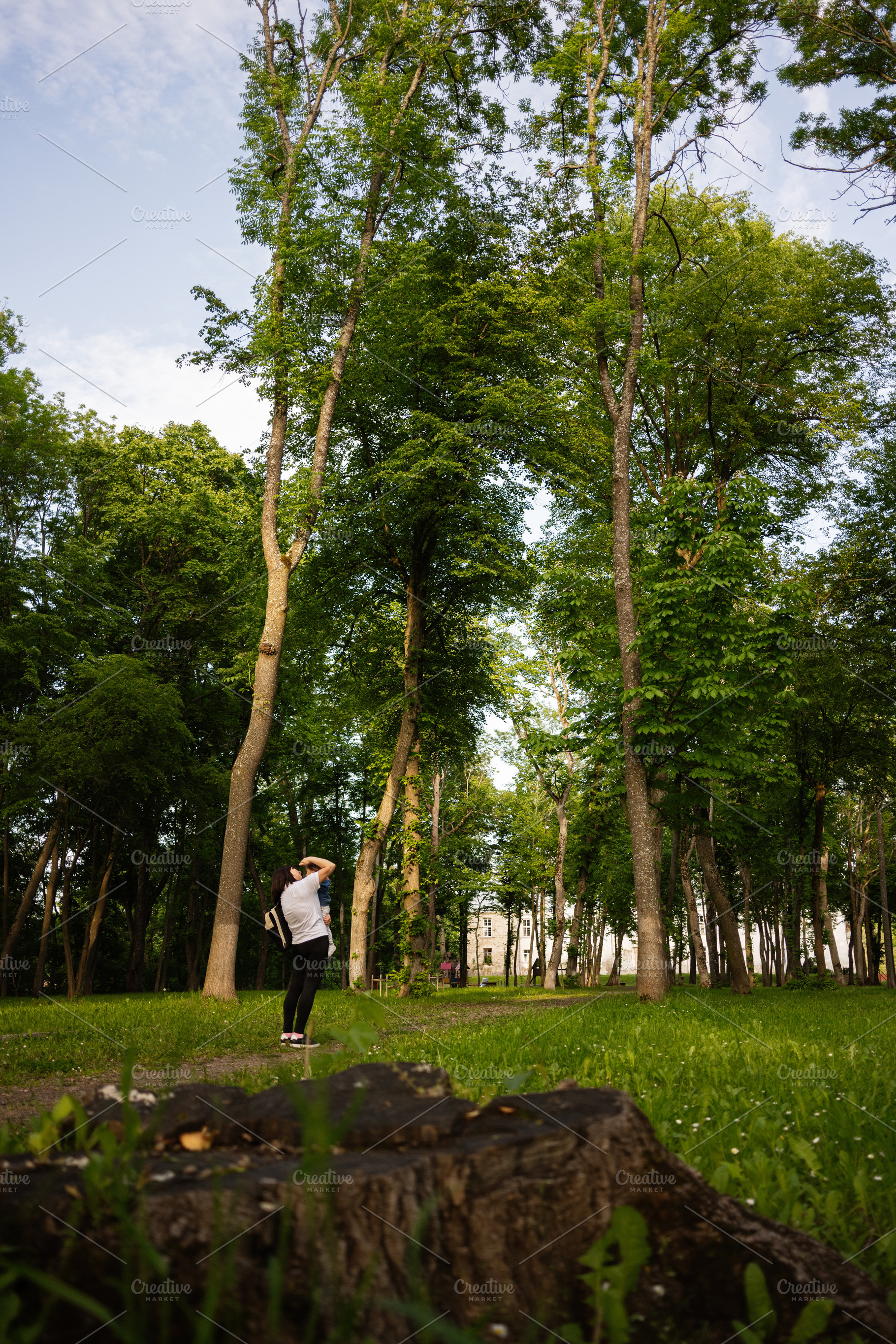 Woman standing in a vibrant park surrounded by tall green trees, a Person Photo by AS photostudio