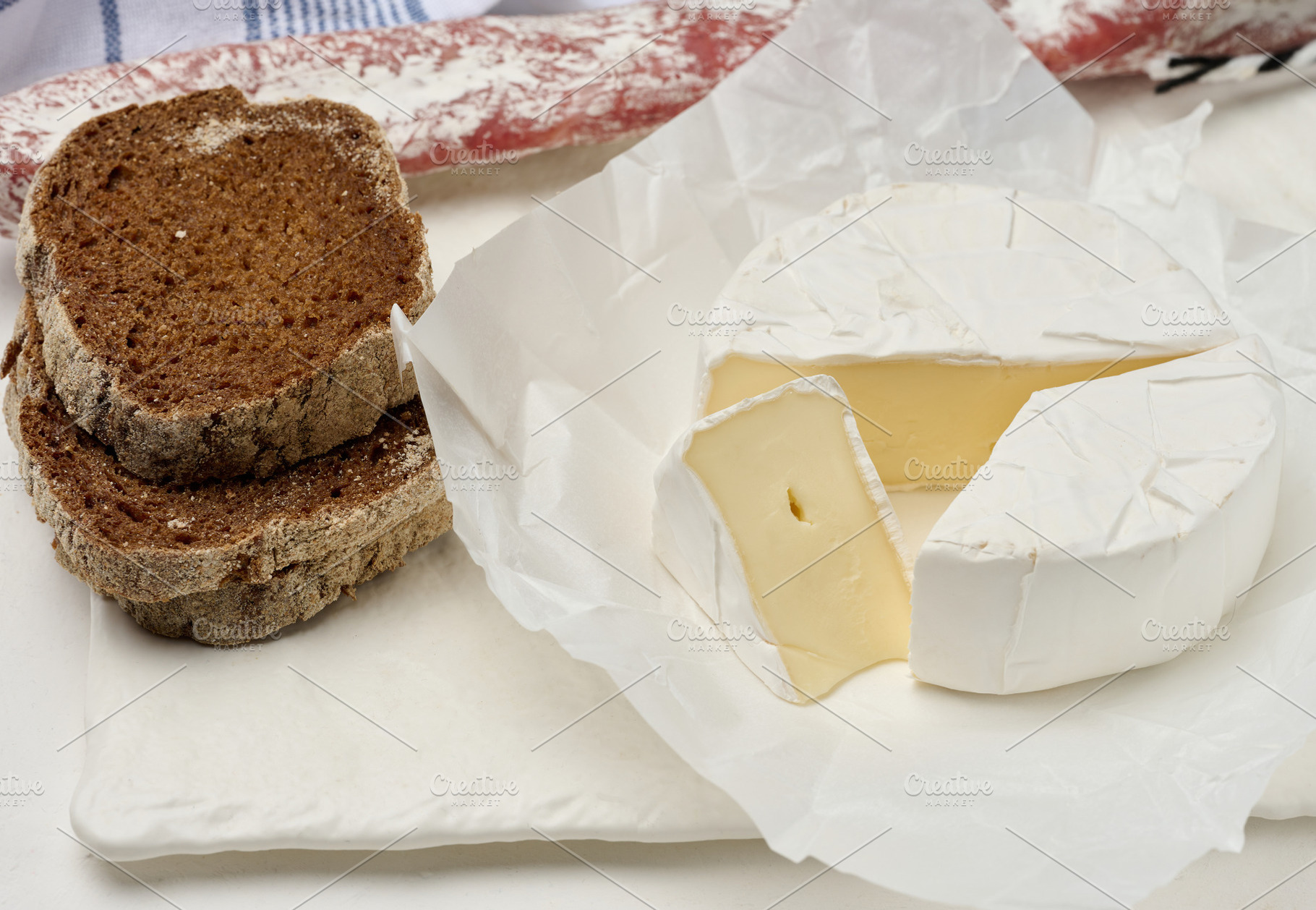 Sliced round head of Camembert cheese on a white board, a Food & Drink Photo by ndanko