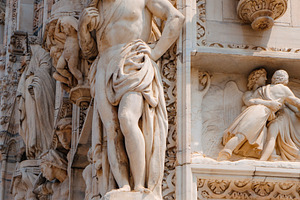 a figure leans on Milans Cathedral corner, a Photo by Nito