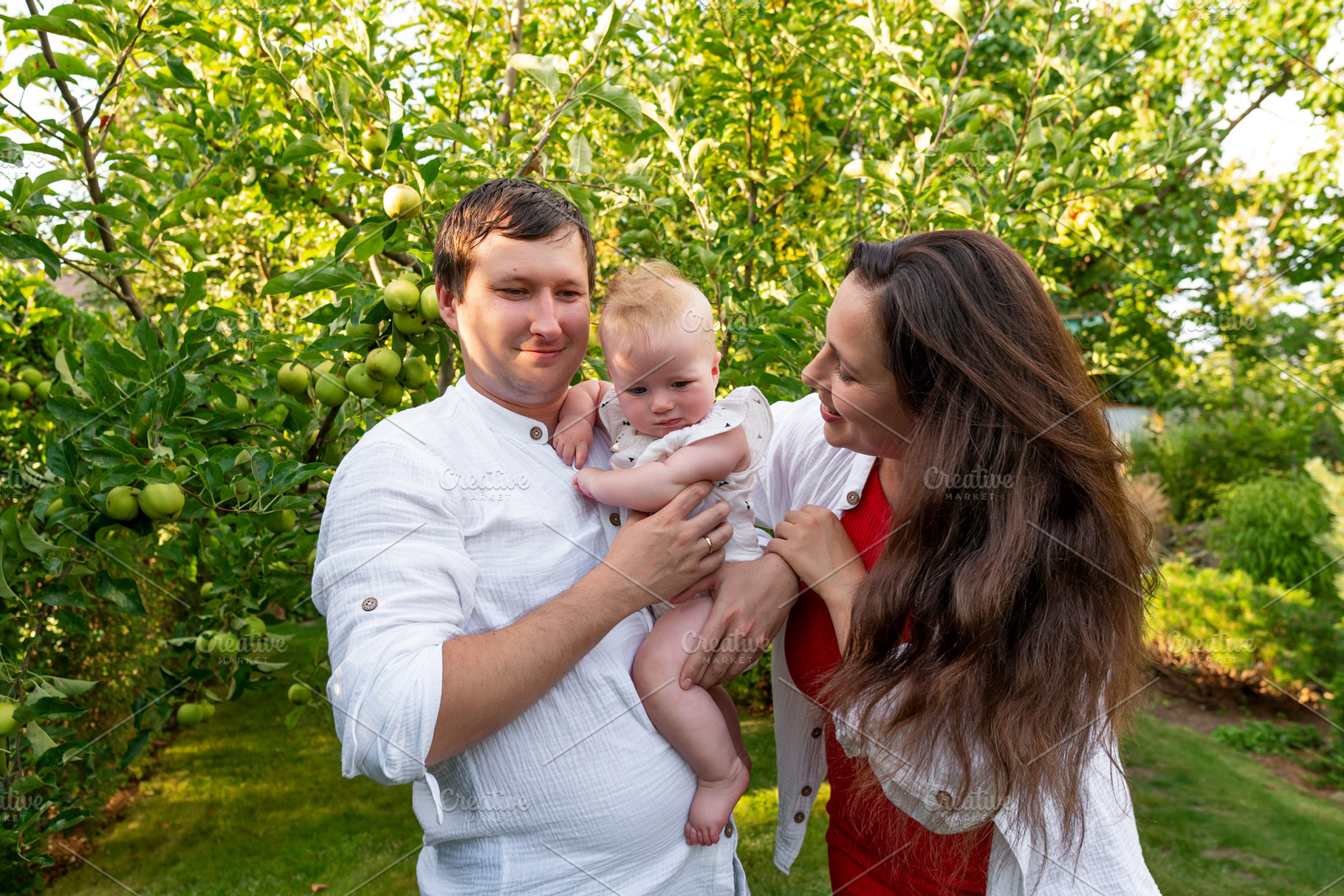 Parents hold curious baby among appl, a Person Photo by Elena Vagengeim