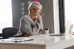 White-haired serious woman working with laptop while sitting at table