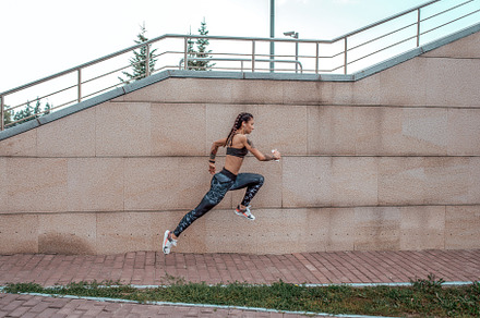 Girl athlete runs in a jump in city containing jogging, people, and wellness
