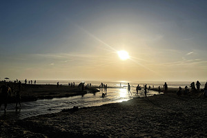 Silhouetted figures enjoying a tranquil sunset at the beach shoreline, a Photo by AS photostudio