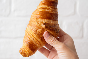 Hand Holding Fresh Croissant Against White Brick Background, a Food & Drink Photo by etorres69