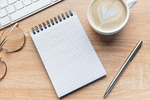 Desk with notepad, keyboard, coffee, pen, and glasses, a School & Education Photo by Olena Rudo