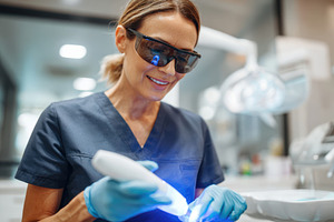 Dentist using blue light tool in modern clinic, a Health & Medical Photo by AlyaAnd