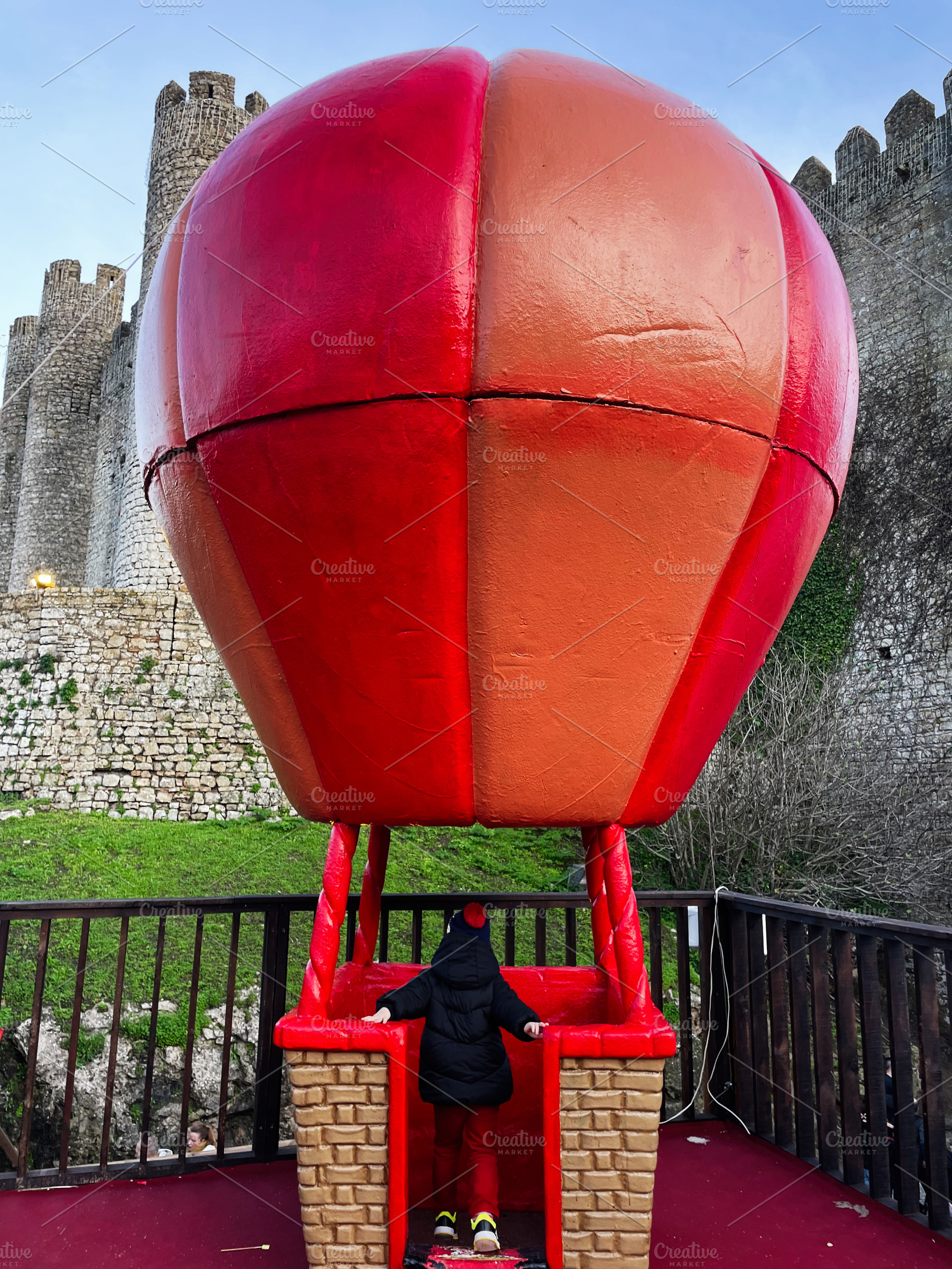 Child exploring a red balloon model near historic castle in Obidos, Portugal, a Photo by AS photostudio