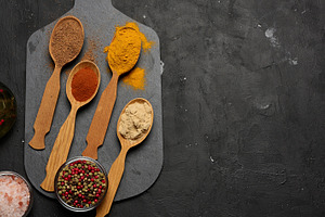 Multicolored ground spices in wooden spoons on a black board, sa, a Food & Drink Photo by ndanko