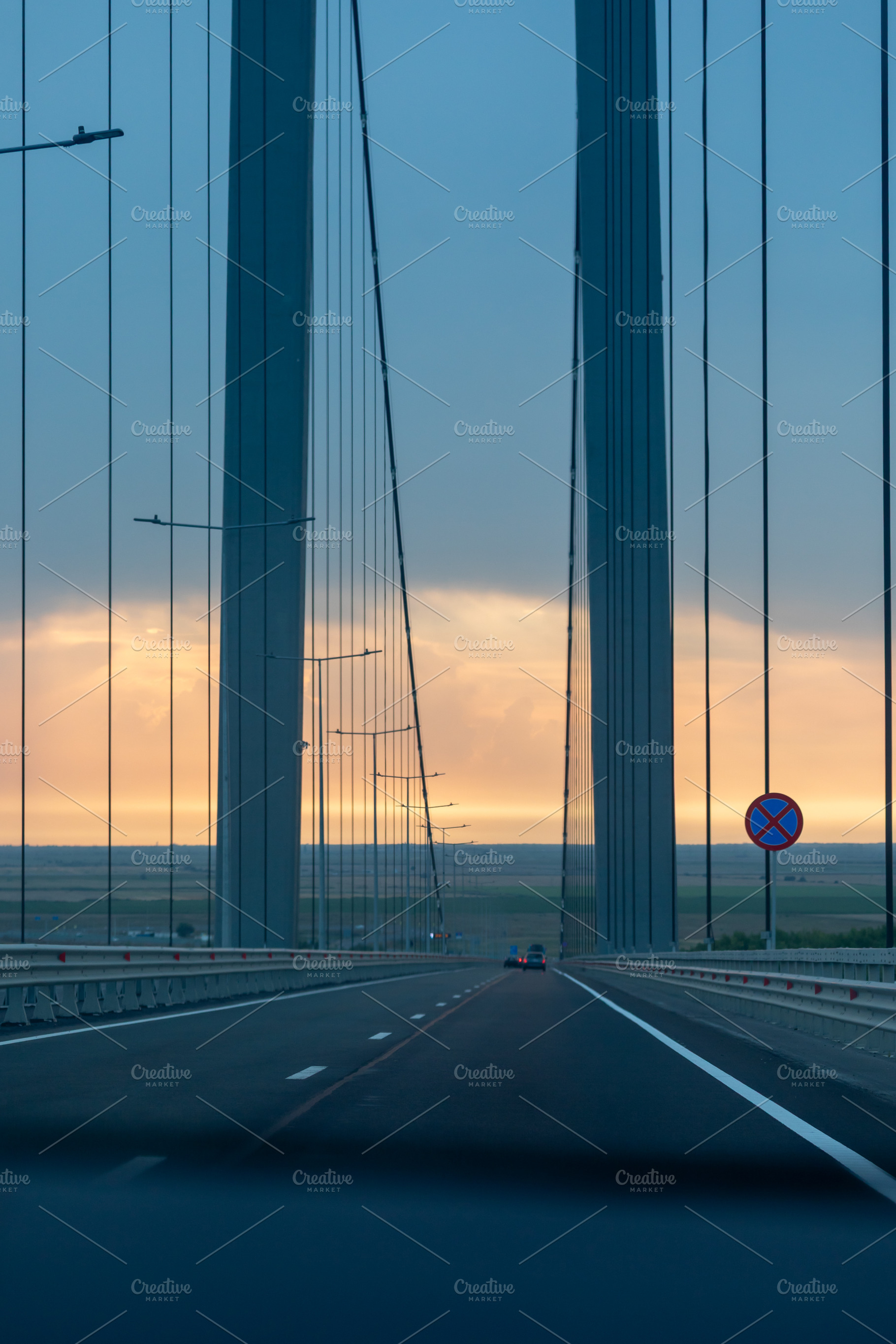 Wide view of a modern suspension bridge at sunset with cars crossing, dramatic, an Architecture Photo by Ales Munt