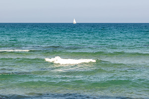 Calm turquoise waves roll onto a sandy beach under a clear blue sky, with a dis, a Nature Photo by Ales Munt