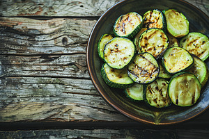 Grilled zucchini pieces in plate on wooden table, a Food & Drink Photo by AlyaAnd