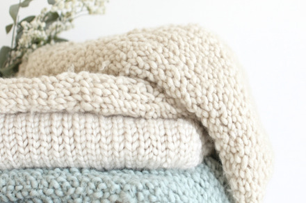 Pastel-colored knitted blankets stacked in basket on white backg, a Photo by Dvoevnore photos