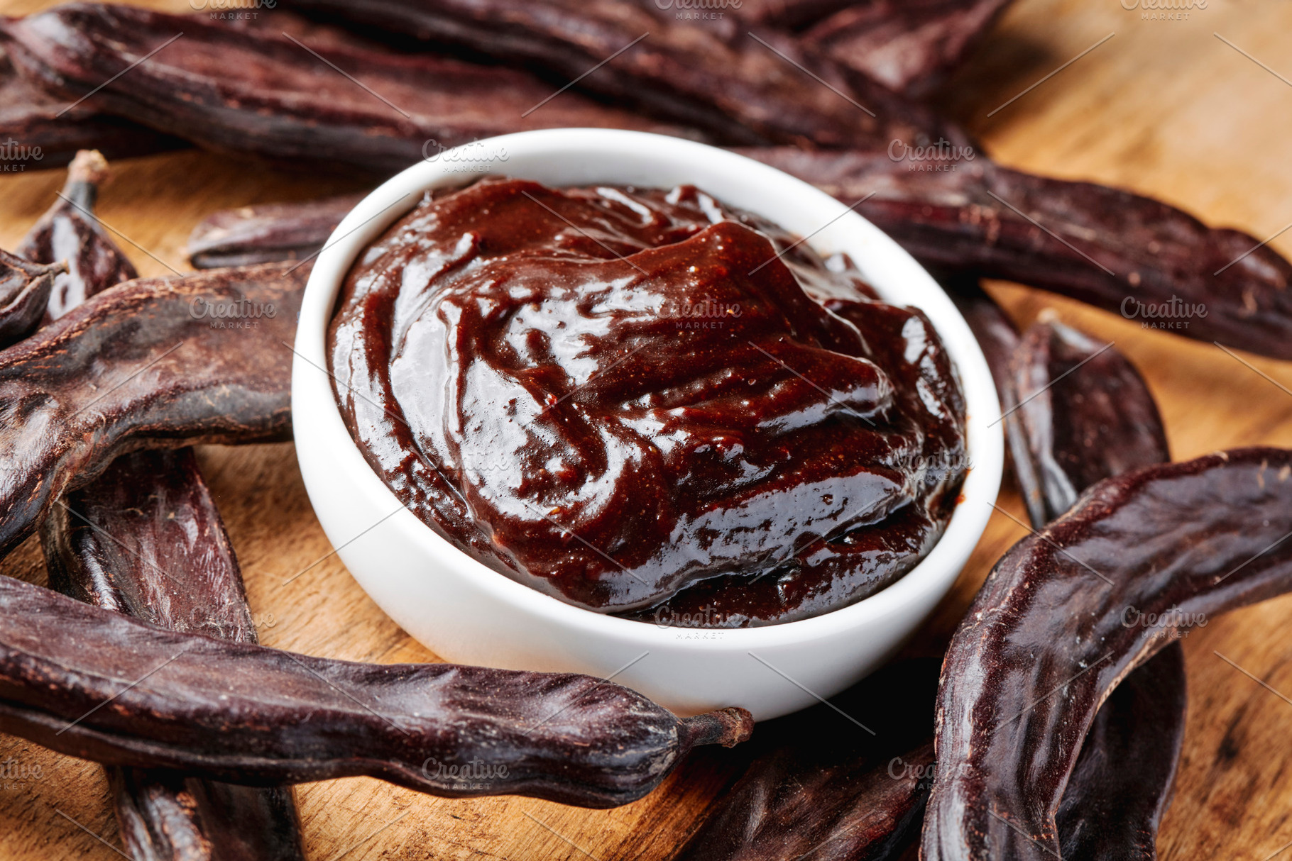 carob cream in a bowl among pods on a wooden table, a Photo by Nito