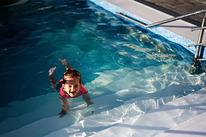 Child swimming and smiling in a clear blue outdoor pool on a sunny day, a Photo by AS photostudio