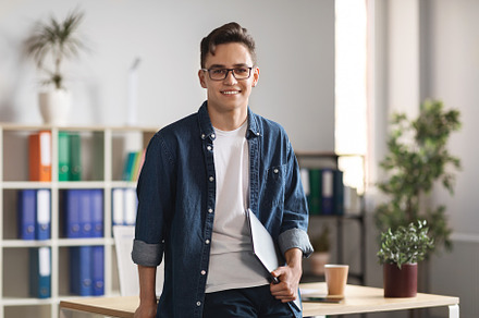 Portrait Of Handsome Young Male Entrepreneur Holding Laptop And Posing In Offic