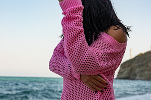 Woman in a pink mesh sweater standing on a sandy beach near the ocean, serene n, a Person Photo by Ales Munt