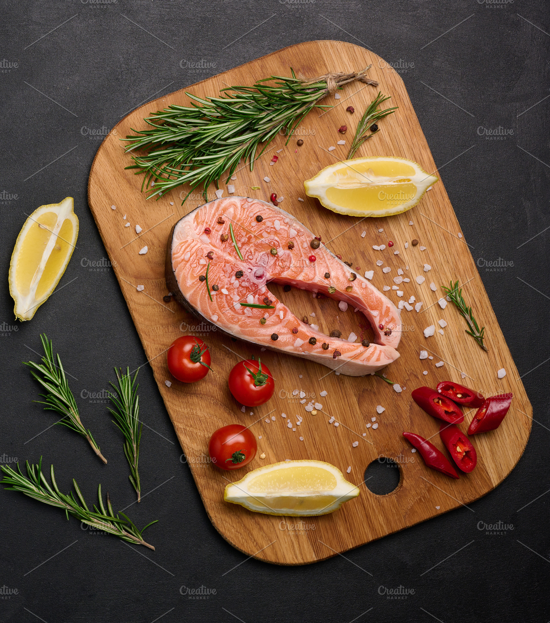 Raw salmon steak on a wooden cutting board, lemon slices, spices, a Food & Drink Photo by ndanko