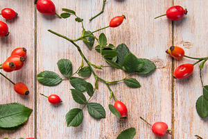 Rosehip berries and leaves arranged on rustic wooden table, a Food & Drink Photo by Olena Rudo