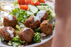 Person holding plate of falafel with hummus and fresh salad, a Food & Drink Photo by etorres69