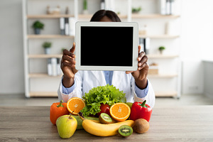 Black nutritionist holding digital tablet with blank screen, demonstrating mock, a Person Photo by Prostock-Studio