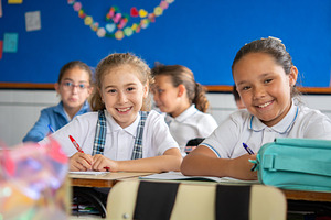 Smiling Elementary School Girls Sitting at Desks in Classroom During Lesson, a School & Education Photo by etorres69