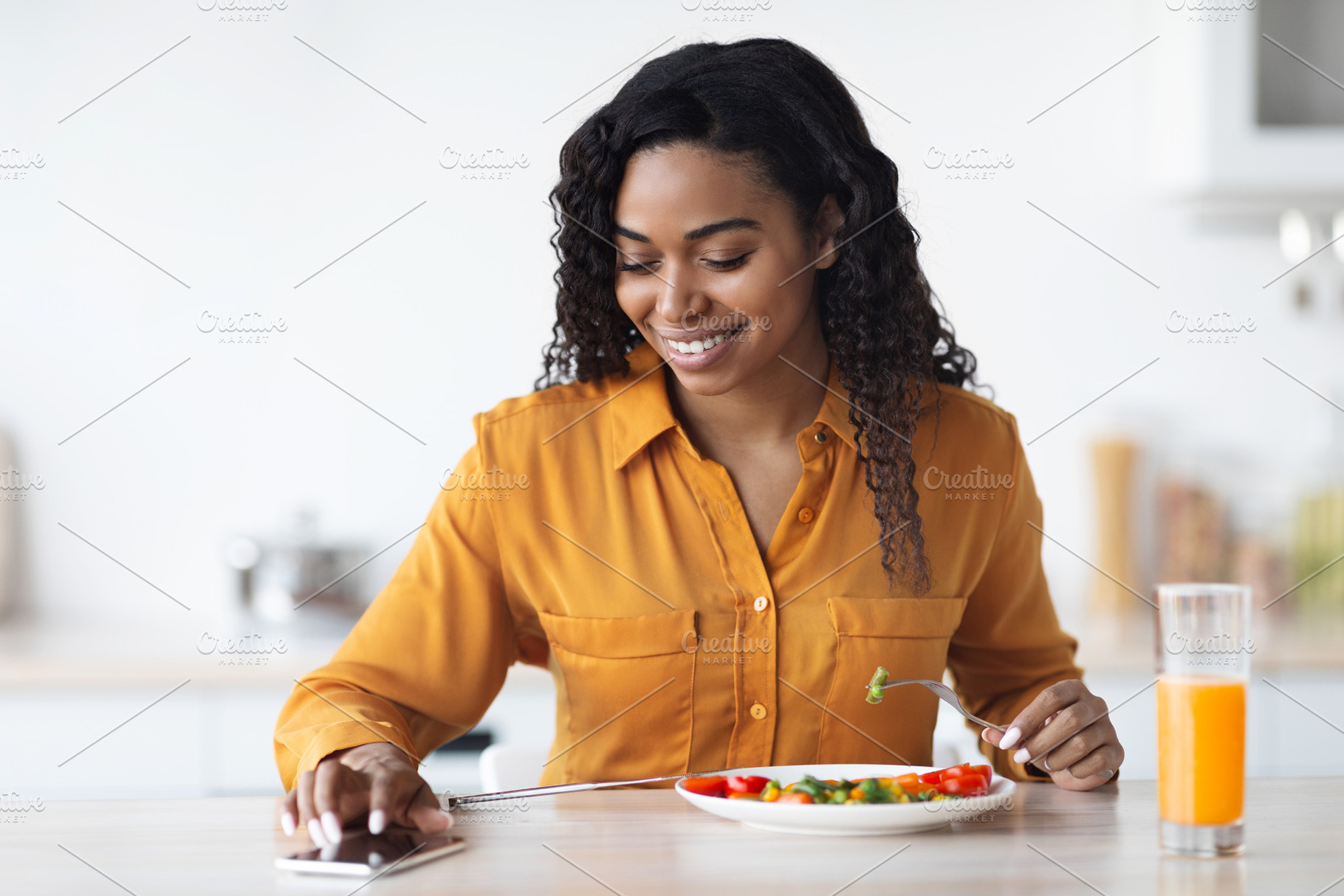 Cheerful african american woman having lunch, using smartphone, a Photo by Prostock-Studio