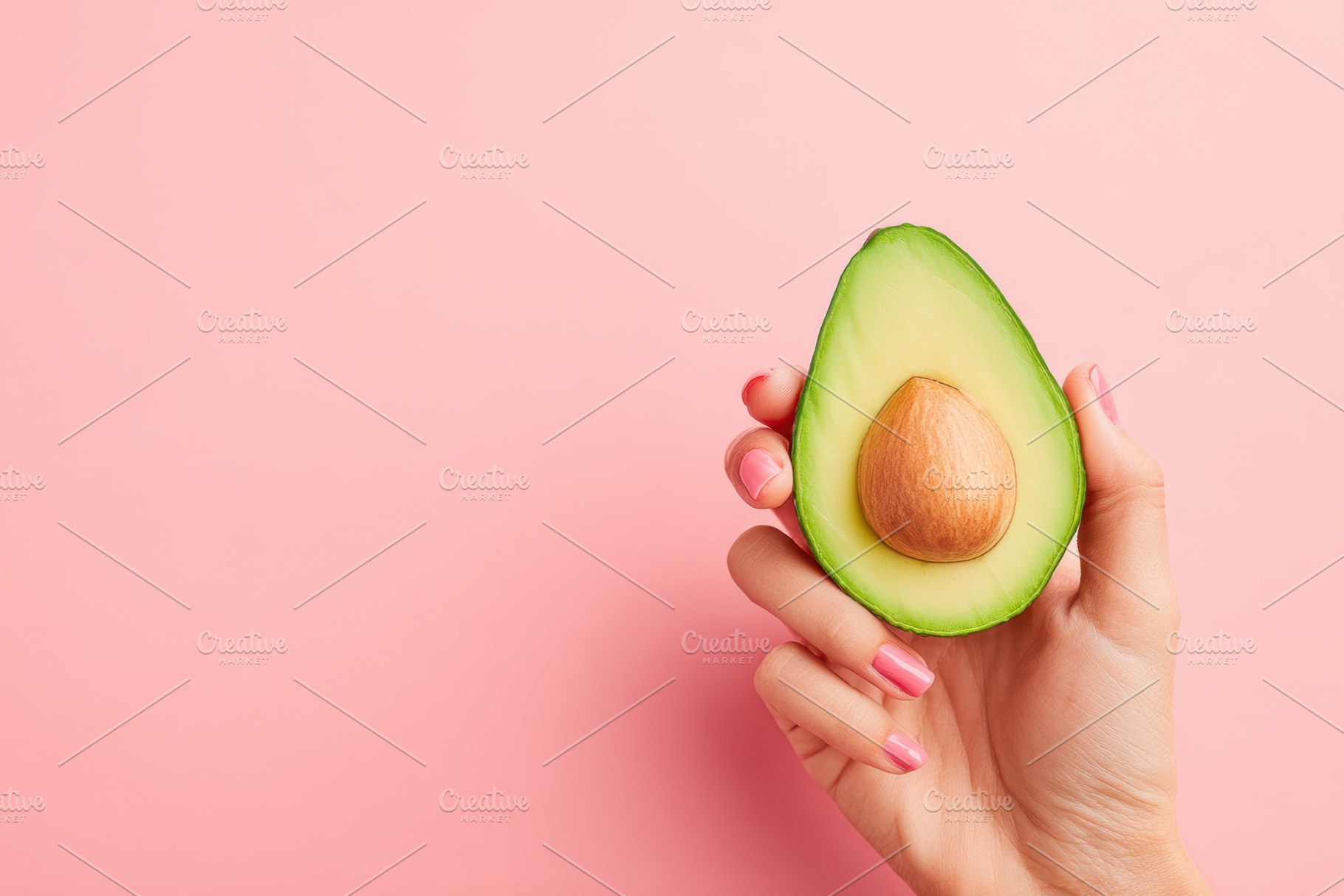 Hand holding a halved avocado on pink background, a Food & Drink Photo by AlyaAnd