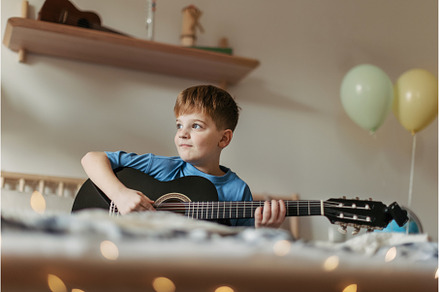 Happy boy playing on the guitar in, a School & Education Photo by HalfPoint
