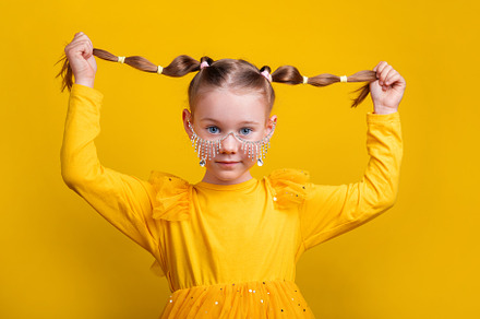 Playful girl in yellow dress and jeweled face accessory holding