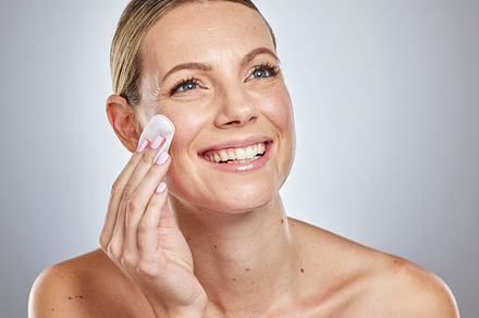 Woman, beauty studio and skincare with cotton pad, cleaning and dermatology health by backdrop. Model, skin wellness and cosmetic clean for glow, facial or natural exfoliate by grey studio background, a Photo by Peopleimages.com