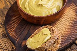 Sweet pistachio cream spread on bread with wooden bowl and knife