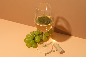 Glass of wine, corkscrew and grape on beige and light brown back, a Food & Drink Photo by AtlasStudio PRO